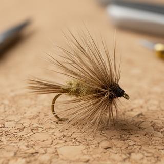 Elk Hair Caddis fly in close-up with tan body and rough deer hair wing on a cork mat